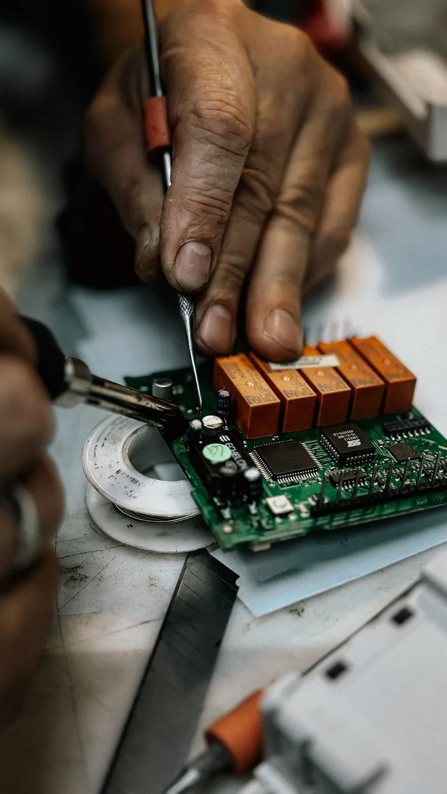 Hands soldering a prototype circuit board with orange relays